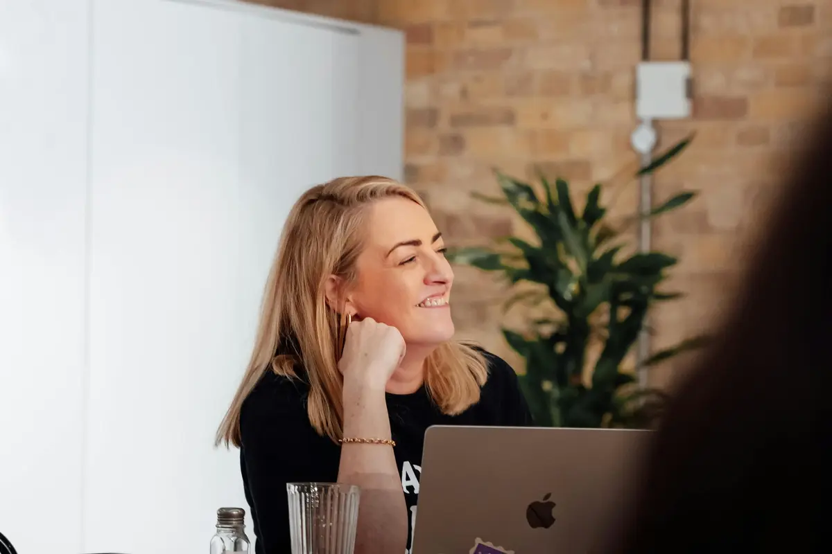 Een vrouw luistert lachend tijdens een gesprek, met haar laptop voor zich